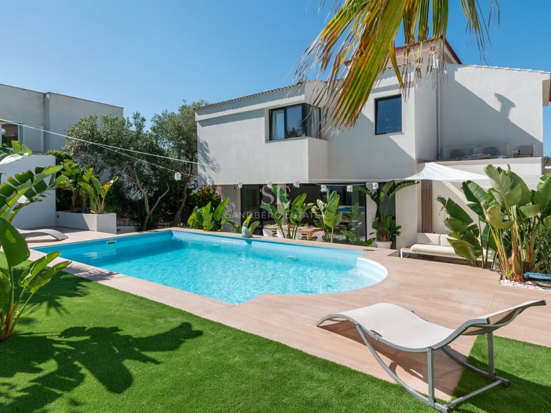 Villa blanche moderne avec piscine bleue, transat, pelouse verte et plantes tropicales par temps clair.