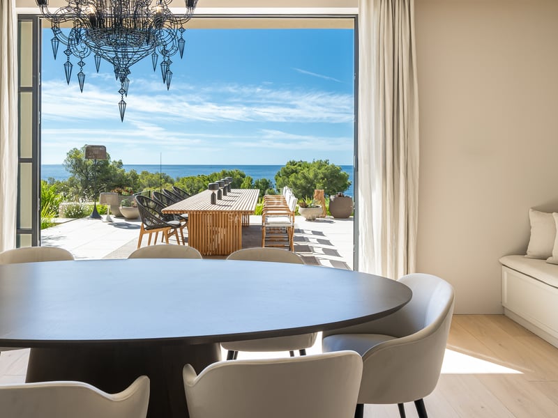 Salle à manger avec table en bois sombre s'ouvrant sur une terrasse ensoleillée avec vue sur la Méditerranée.