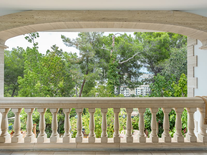 Balustrade en pierre beige sous une arche en pierre surplombant des arbres verts et des bâtiments au loin.