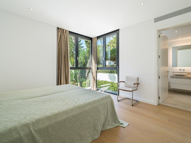 Chambre de maître lumineuse avec parquet, fenêtres d'angle et salle de bain moderne attenante.