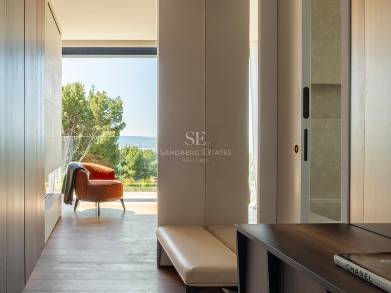 Couloir moderne, parquet en bois, fauteuil terracotta et grandes baies vitrées offrant une vue sur mer et pins.