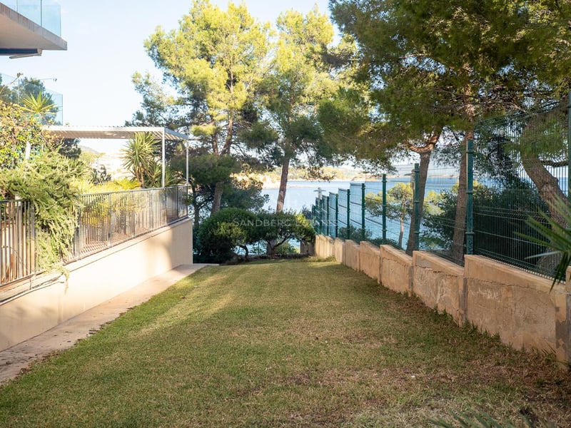 Une pelouse soignée entourée de pins et d'une clôture métallique, surplombant la mer Méditerranée turquoise.