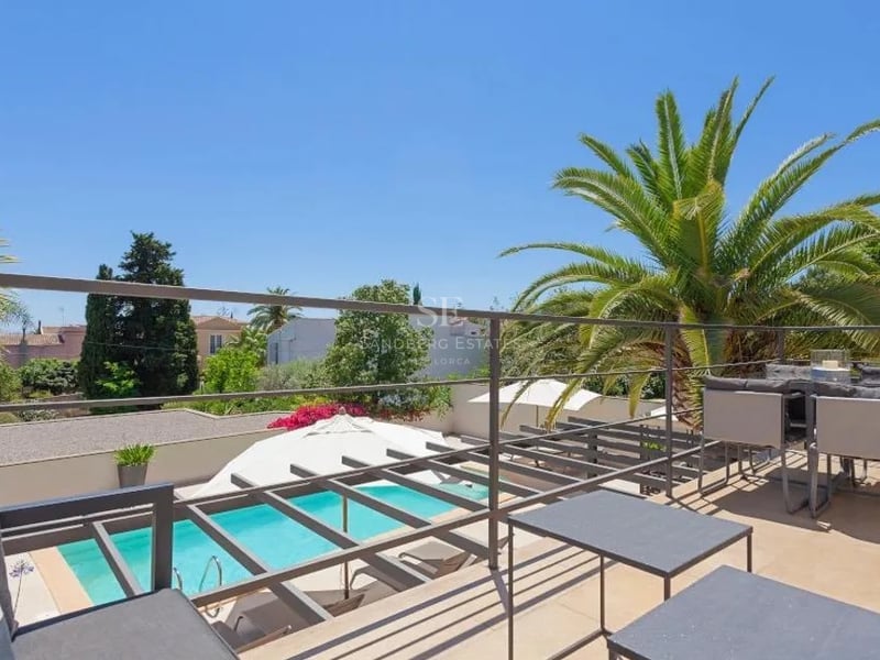 Terrasse surélevée avec mobilier en métal gris, vue sur une piscine turquoise et des palmiers sous un ciel bleu azur.