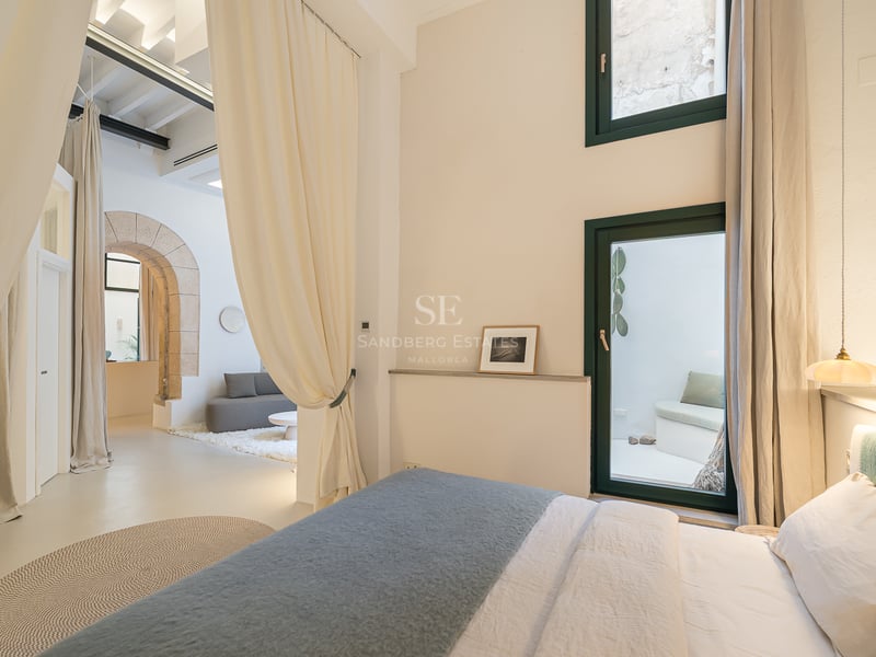Chambre de luxe avec drapés blancs, arche en pierre historique et vue sur un salon minimaliste.