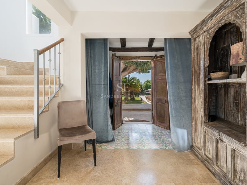 Hall d'entrée avec escalier en pierre, armoire en bois ancienne et portes ouvertes sur le jardin.
