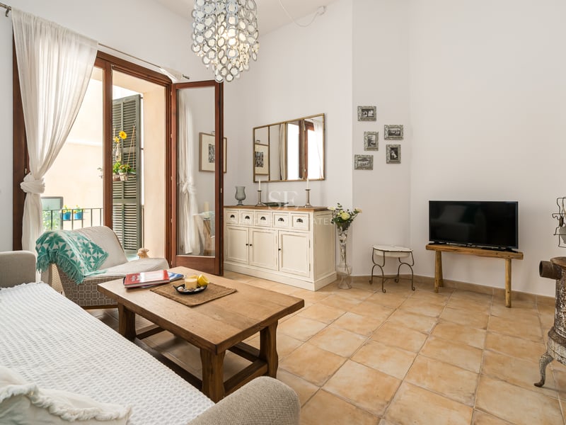 Salon spacieux avec sol en terre cuite, table basse en bois et grandes portes ouvrant sur un balcon.