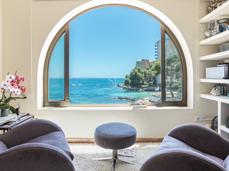 Deux fauteuils en velours face à une grande fenêtre en plein cintre donnant sur une baie méditerranéenne avec des bateaux.