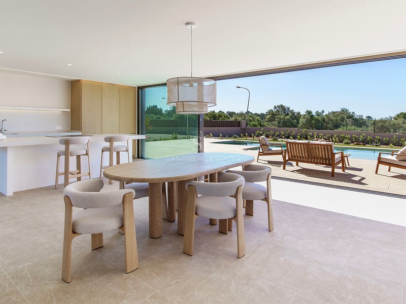 Espace dînatoire en bois clair avec baies vitrées ouvertes sur une terrasse et une piscine ensoleillée.