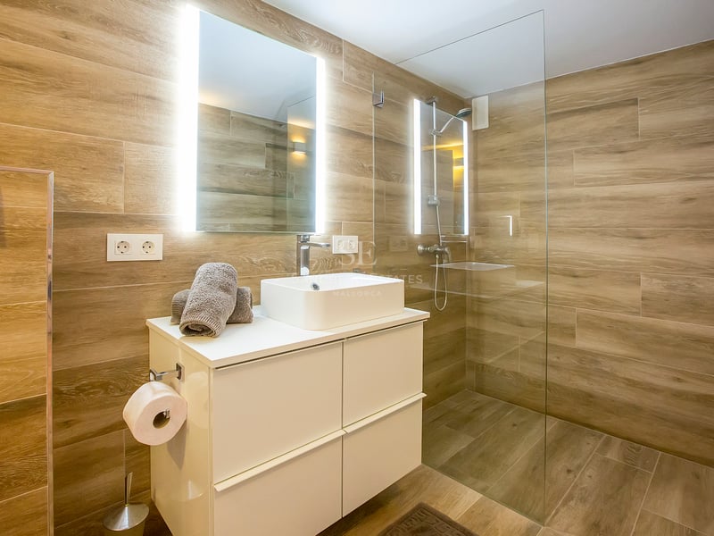 Salle de bains contemporaine avec carrelage effet bois, douche à l'italienne et vasque blanche avec miroir rétroéclairé.