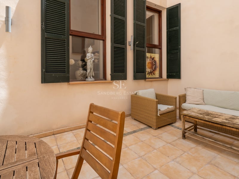Terrasse privée avec carrelage en terre cuite, volets majorquins verts et mobilier en bois et rotin.
