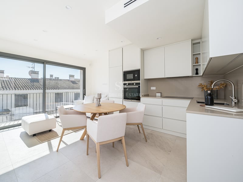 Cuisine minimaliste blanche avec table en bois, chaises rembourrées et grandes baies vitrées.