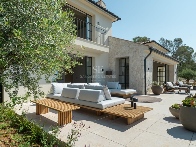 Salon d'extérieur contemporain sur terrasse en pierre avec olivier, mobilier en bois et façade de la villa.
