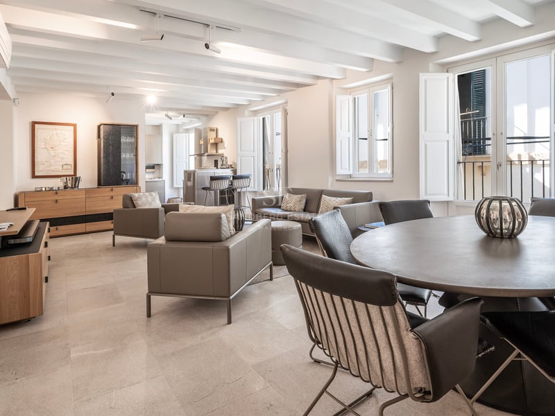 Salon spacieux avec plafonds à poutres blanches, meubles en cuir gris et table à manger ronde.