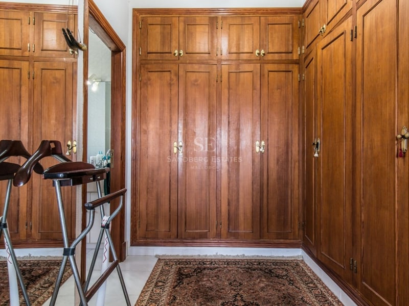 Dressing avec placards intégrés en bois du sol au plafond, tapis persan et valet de nuit.
