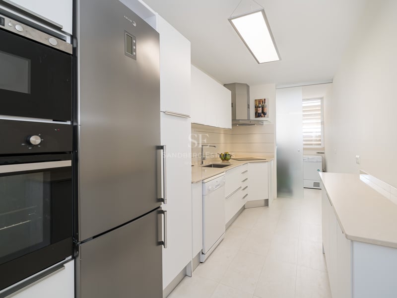 Une cuisine moderne en longueur avec des meubles blancs et des appareils en acier inoxydable.