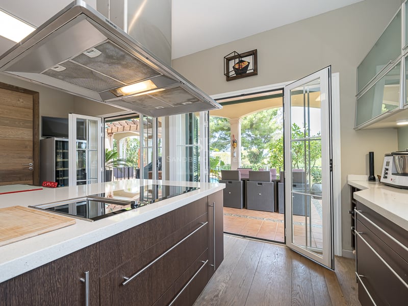 Cuisine contemporaine avec îlot en bois sombre et quartz blanc, s'ouvrant sur une terrasse dînatoire ensoleillée.