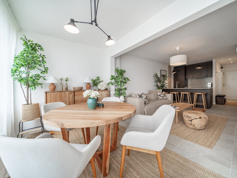 Salle à manger moderne avec table ronde en bois, chaises blanches et vue sur le salon et la cuisine ouverte.