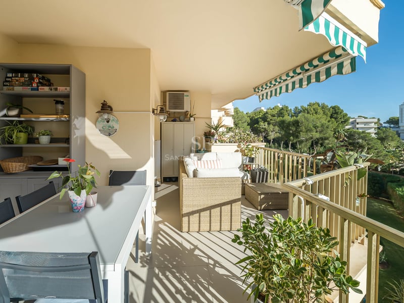 Grand balcon carrelé avec table à manger extérieure, canapé en osier et store à rayures vertes et blanches.