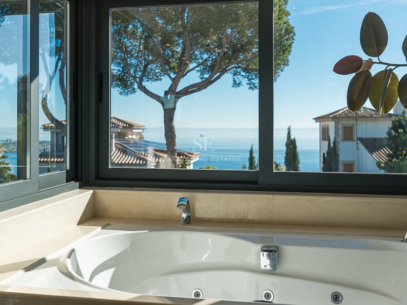 Baignoire balnéo blanche devant une grande baie vitrée offrant une vue panoramique sur la mer Méditerranée.