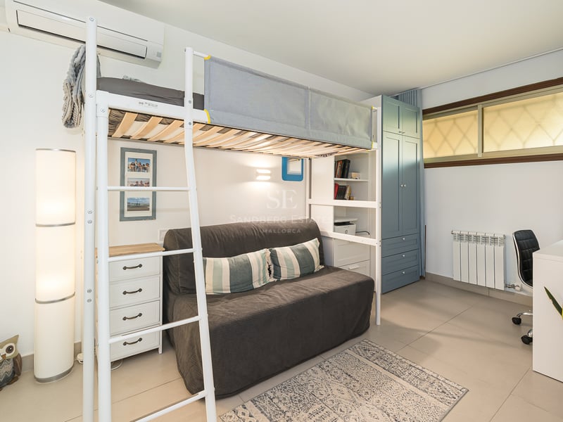 Lit mezzanine en métal blanc au-dessus d'un canapé gris, à côté d'un bureau et d'une armoire bleue.
