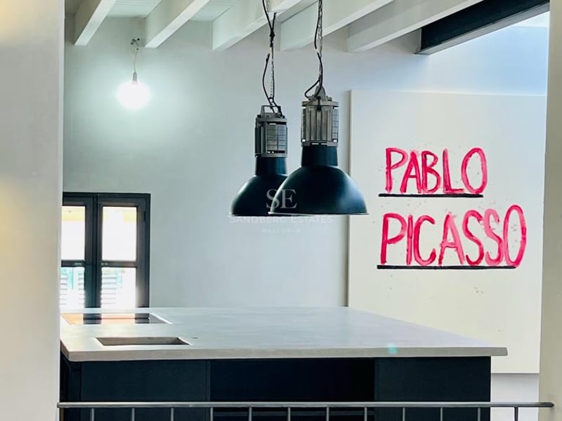 Îlot de cuisine moderne avec plan de travail gris, suspensions industrielles noires et plafond à poutres blanches.