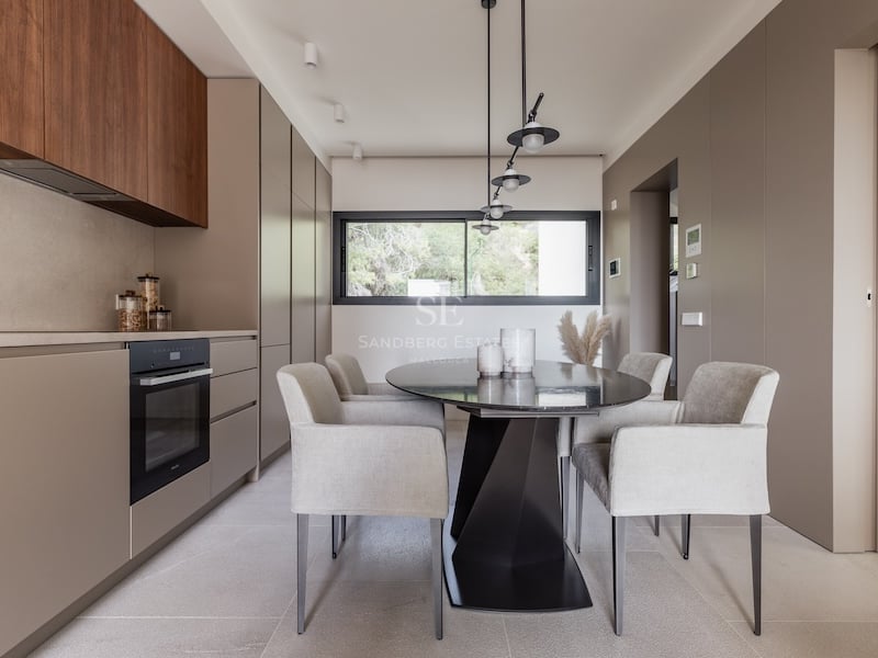 Salle à manger moderne avec table ovale noire, fauteuils gris et placards taupe sous des suspensions design.