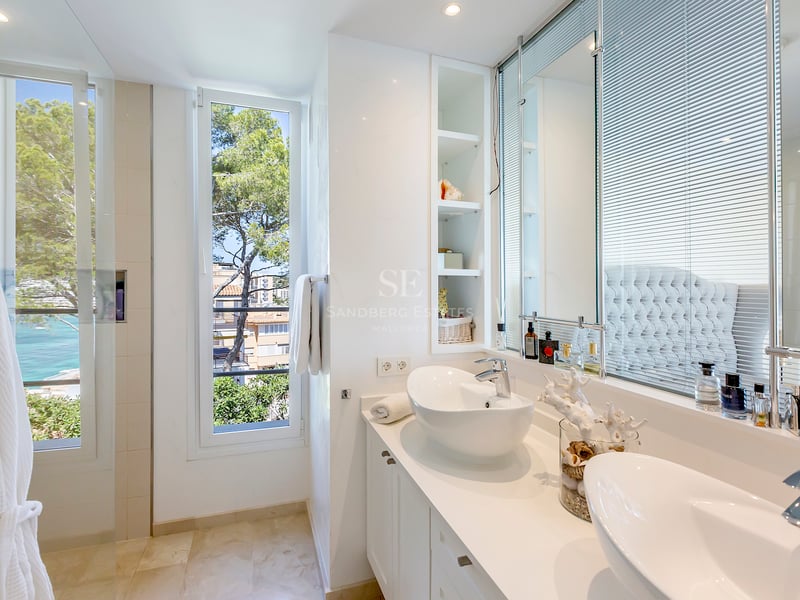 Salle de bain lumineuse avec deux vasques à poser blanches et fenêtre donnant sur la mer et des pins.