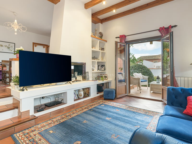 Salon avec sol en terre cuite, poutres en bois apparentes et portes ouvrant sur une terrasse ensoleillée.