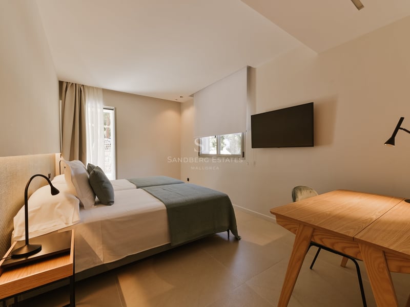 Chambre minimaliste avec lits jumeaux, linge de maison gris, bureau en bois et télévision murale.