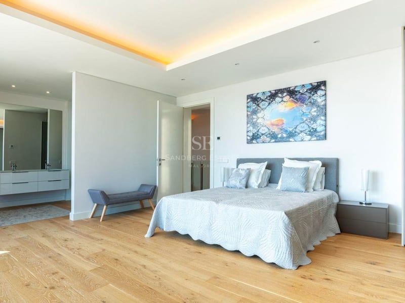 Grande chambre parentale moderne avec parquet en bois clair, lit double et espace coiffeuse attenant.