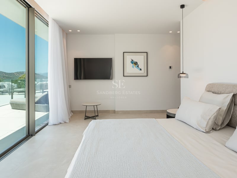 Chambre moderne avec grand lit et baies vitrées coulissantes ouvrant sur une terrasse ensoleillée.