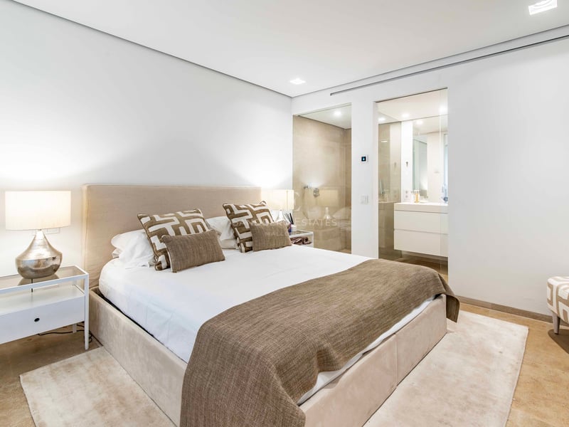 Chambre moderne aux tons neutres, lit rembourré et salle de bains vitrée avec sol en pierre naturelle.