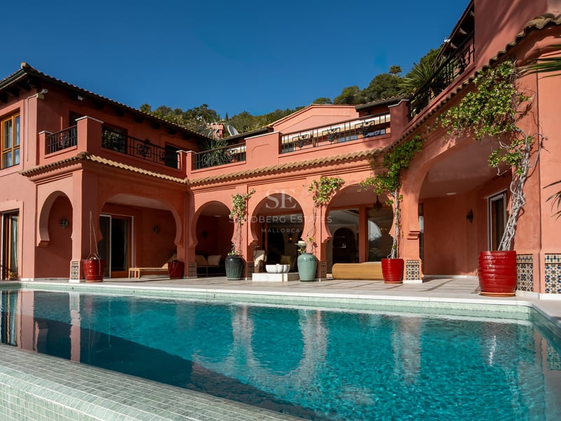 Grande piscine turquoise devant une villa terre cuite aux arches traditionnelles et terrasses ensoleillées.