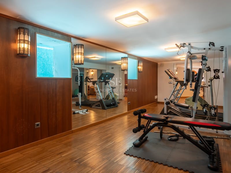 Salle de sport à domicile avec parquet, murs miroir, tapis de course et banc de musculation.