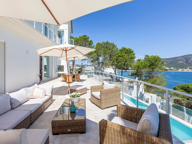 Grande terrasse en pierre blanche avec mobilier en rotin, garde-corps en verre et vue sur la mer et les montagnes.