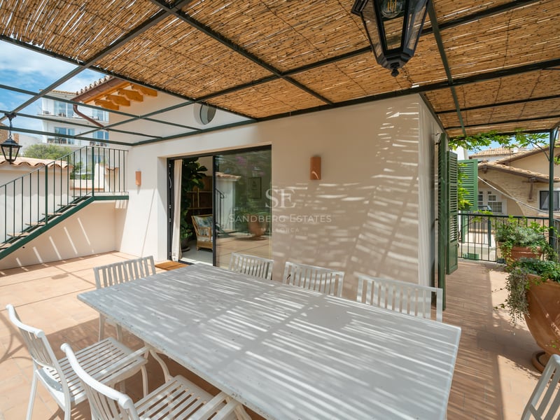 Table et chaises en bois blanc sous une pergola en canisse avec une lanterne traditionnelle sur une terrasse.