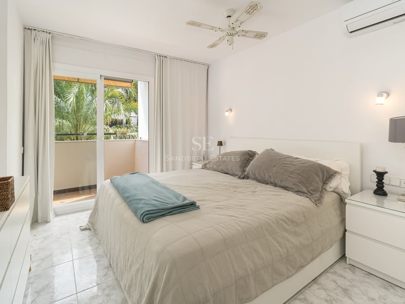 Chambre lumineuse avec lit double, sol en marbre et balcon offrant une vue sur des palmiers.