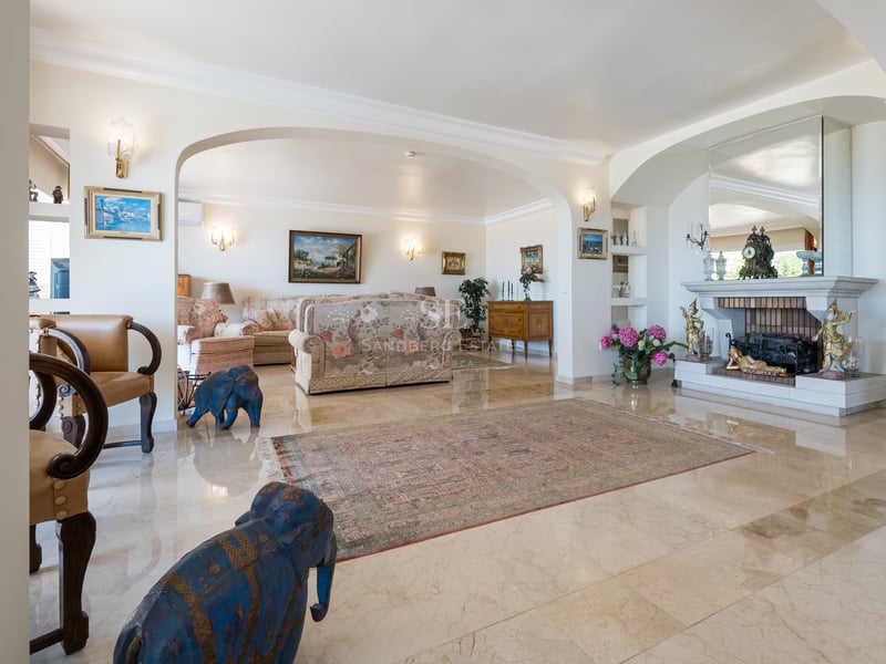 Grand salon avec sols en marbre crème poli, cheminée en pierre et ouvertures voûtées.