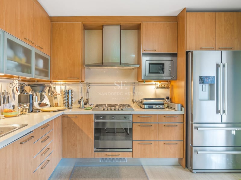 Cuisine contemporaine avec placards en bois clair, appareils en acier inoxydable et éclairage intégré.