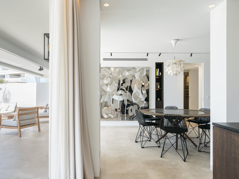 Salle à manger moderne avec table ronde en bois s'ouvrant sur une terrasse ensoleillée avec mobilier de salon.
