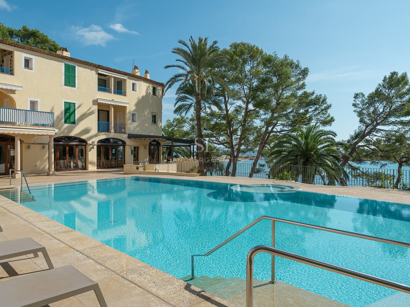 Grande piscine bleue avec terrasse en pierre naturelle surplombant la mer et les pins à côté d'une villa jaune.