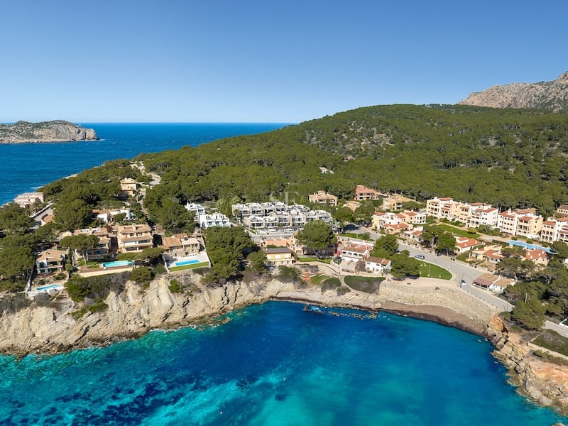 Vue aérienne de villas méditerranéennes sur une falaise dominant une baie turquoise et une forêt luxuriante.