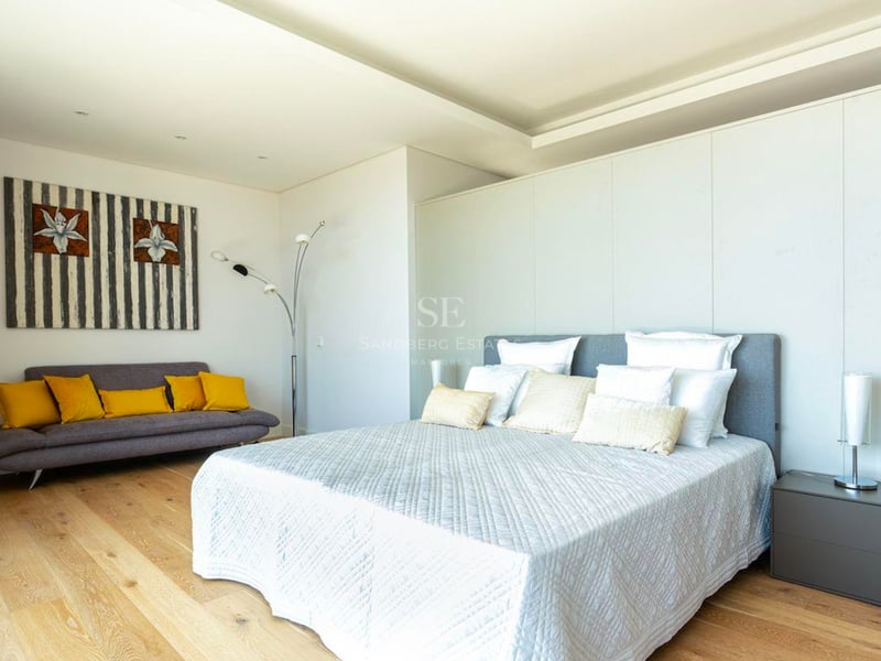 Chambre moderne lumineuse avec grand lit, parquet et canapé gris aux coussins jaunes.