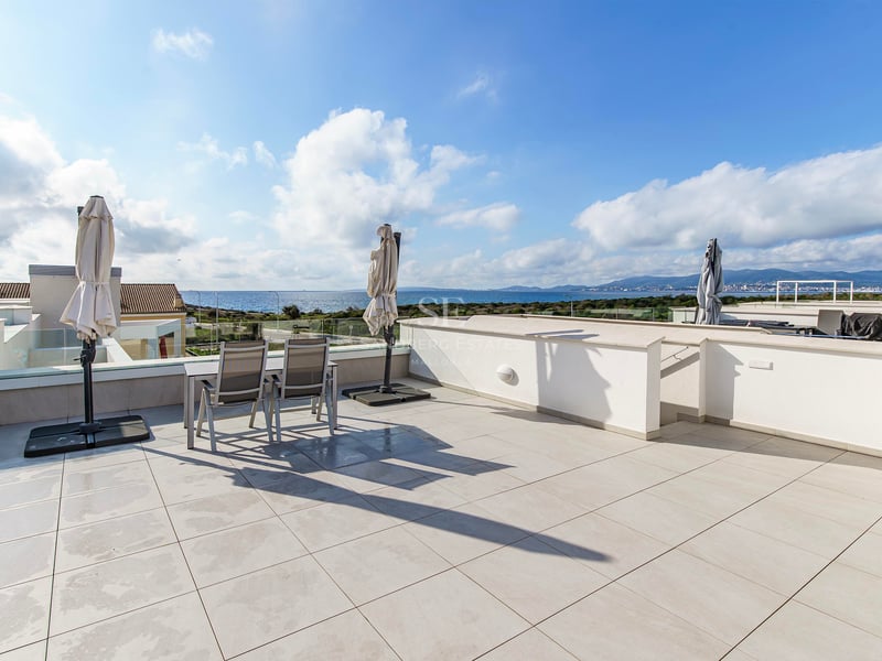 Grande terrasse moderne avec carrelage blanc, garde-corps en verre et coin repas avec vue sur la mer bleue.