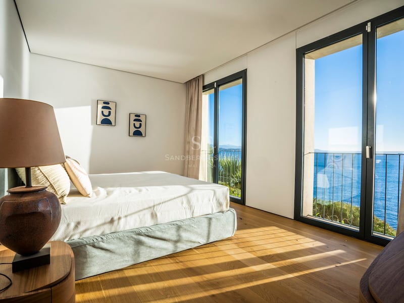 Chambre de maître moderne avec parquet en chêne, baies vitrées et vue sur la mer Méditerranée bleue.