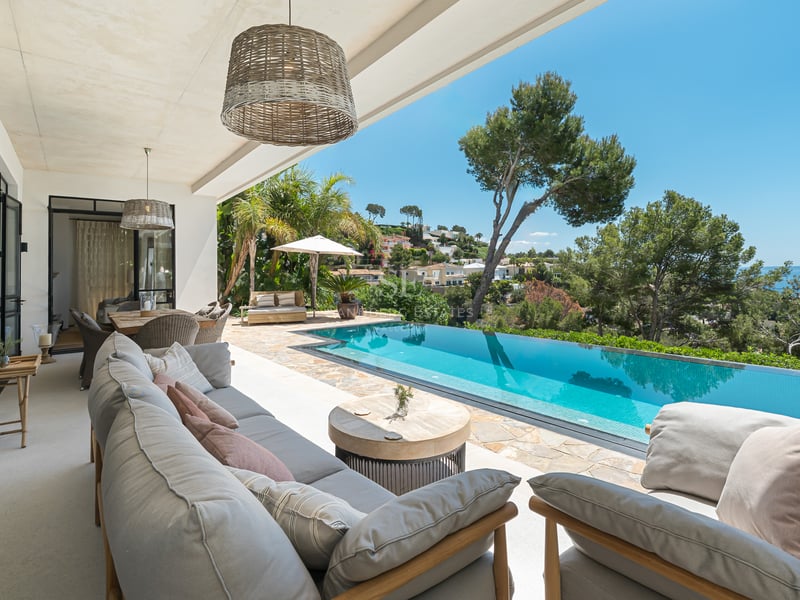 Terrasse couverte avec salon gris donnant sur une piscine à débordement turquoise et la mer Méditerranée.