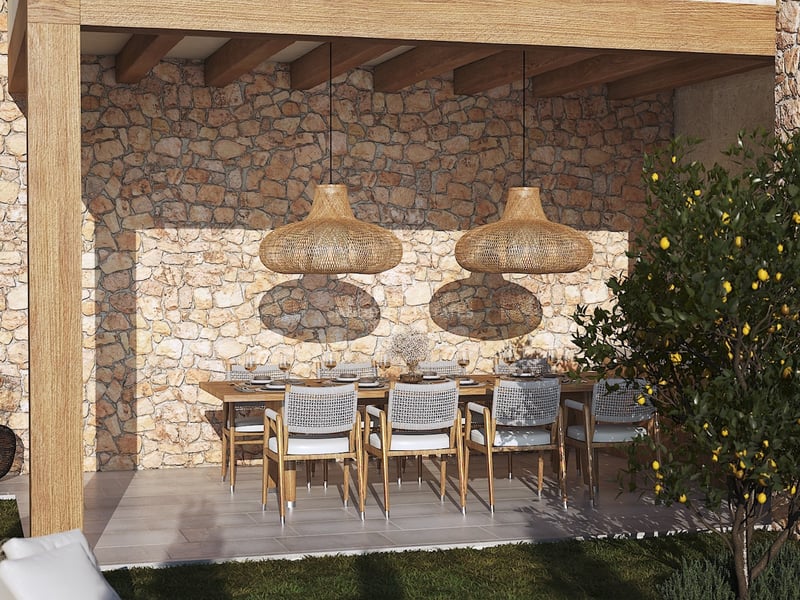 Comedor exterior cubierto con mesa de madera, lámparas de mimbre y pared de piedra natural rústica.
