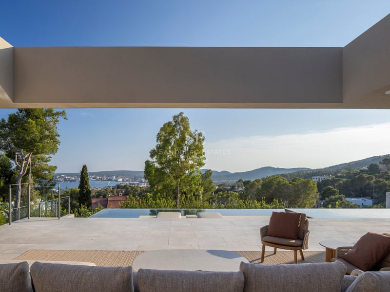Salon extérieur de luxe avec mobilier contemporain sur une terrasse en pierre dominant la piscine et la mer.