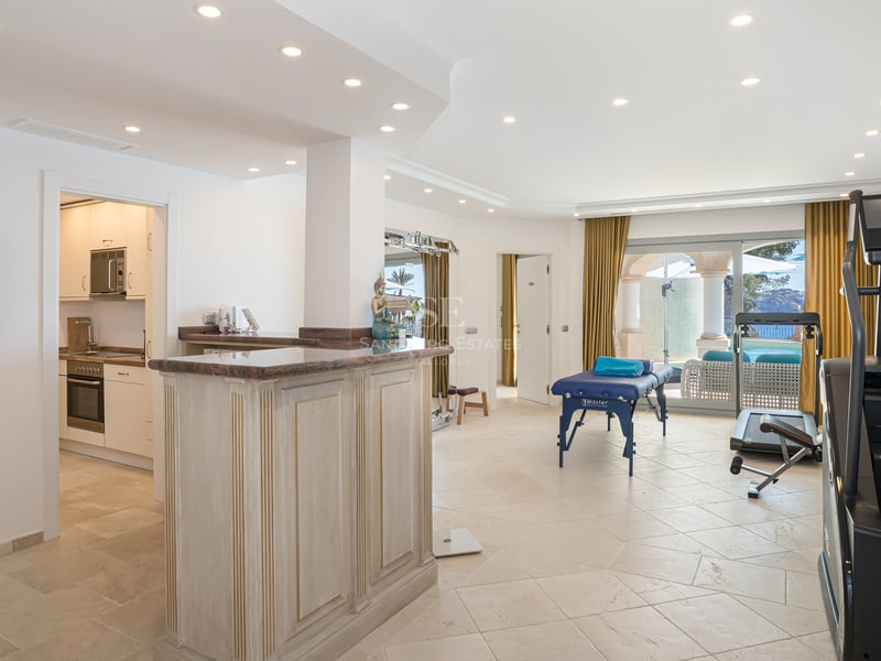 Salle de bien-être lumineuse avec table de massage, équipement de fitness, bar en bois et accès terrasse.