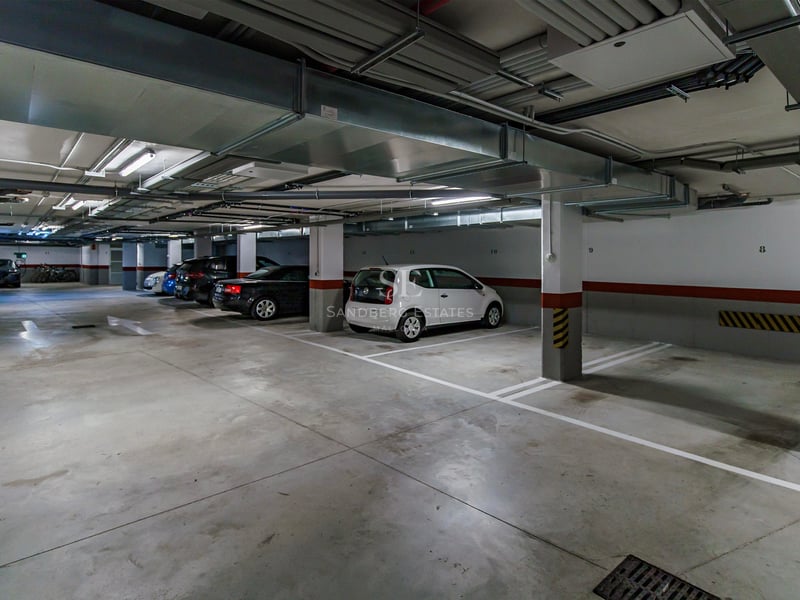 Parking souterrain éclairé avec places numérotées et voitures garées sous des conduits de ventilation.